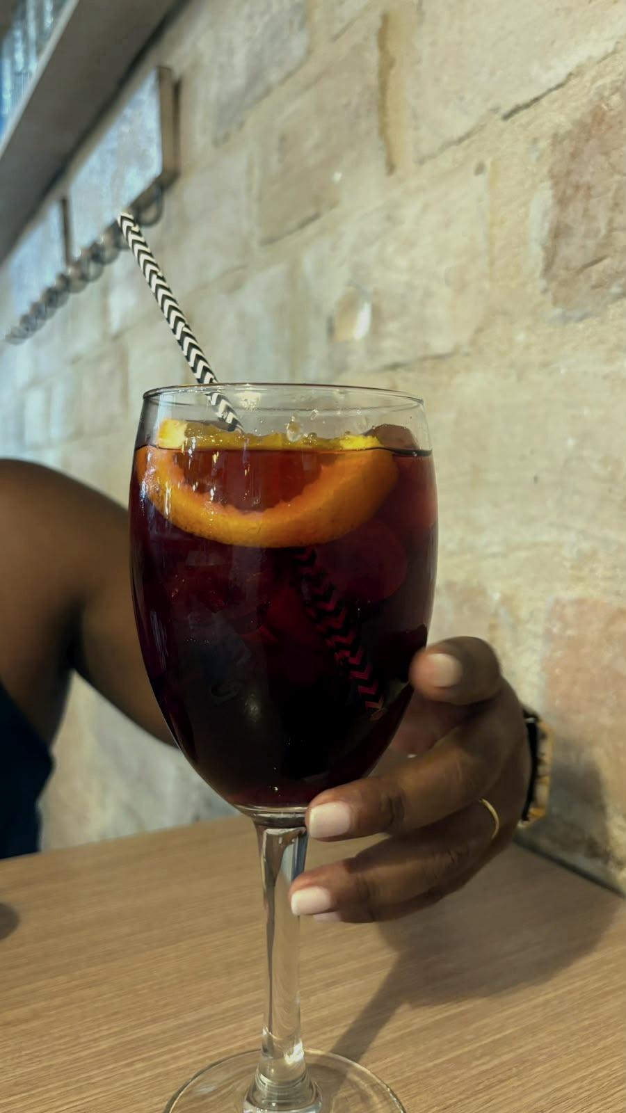 A glass of sangria with a slice of orange, in hand.